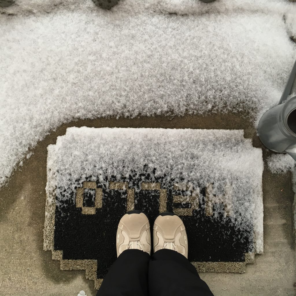 Pieds sur mon tapis d'entrée noir avec l'inscription "Hello" parsemé de neige
