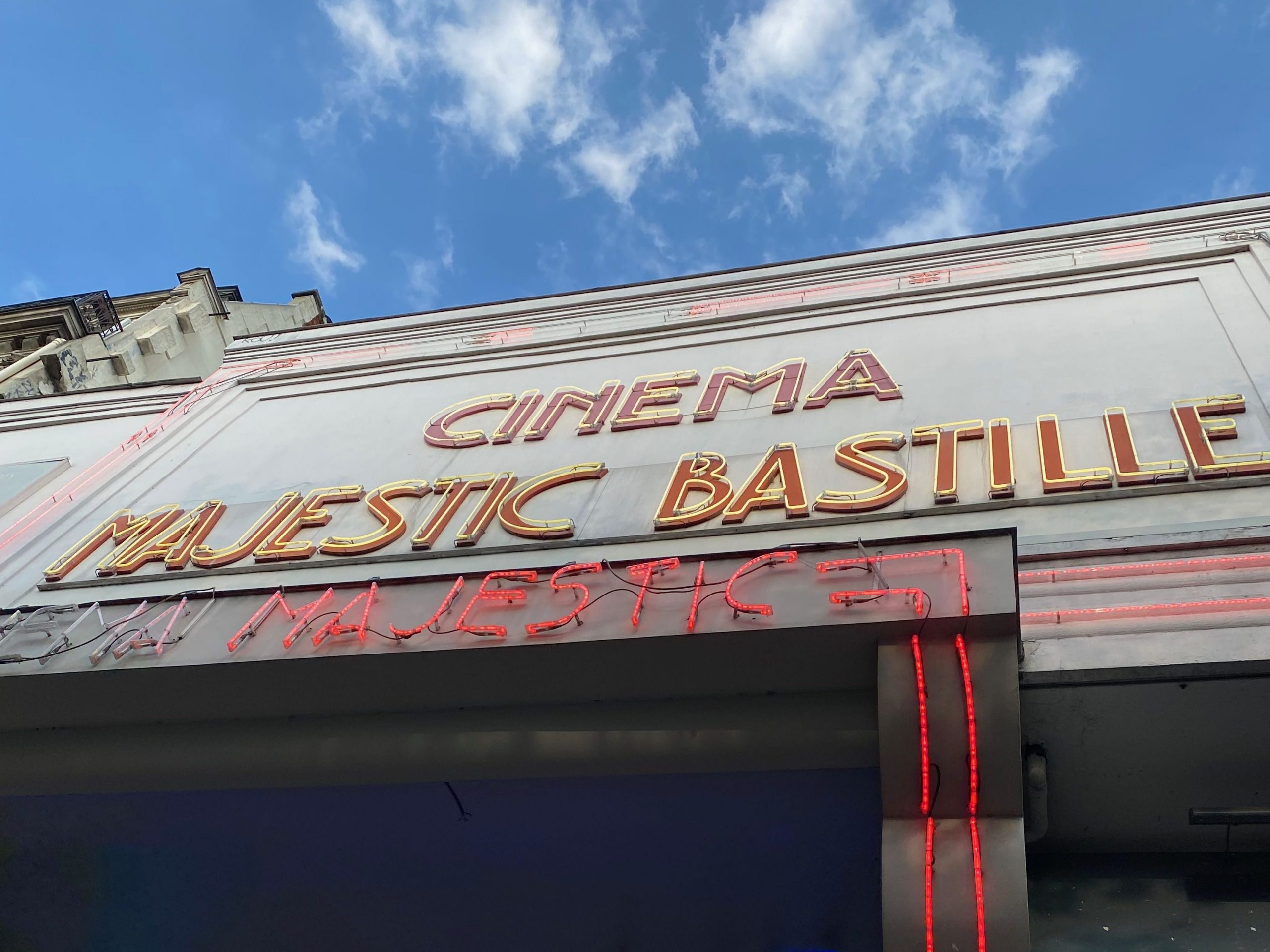 Facade du cinéma, Cinéma Majestic Bastille en néon jaune avec un fond rouge et le ciel bleu en arrière plan.
