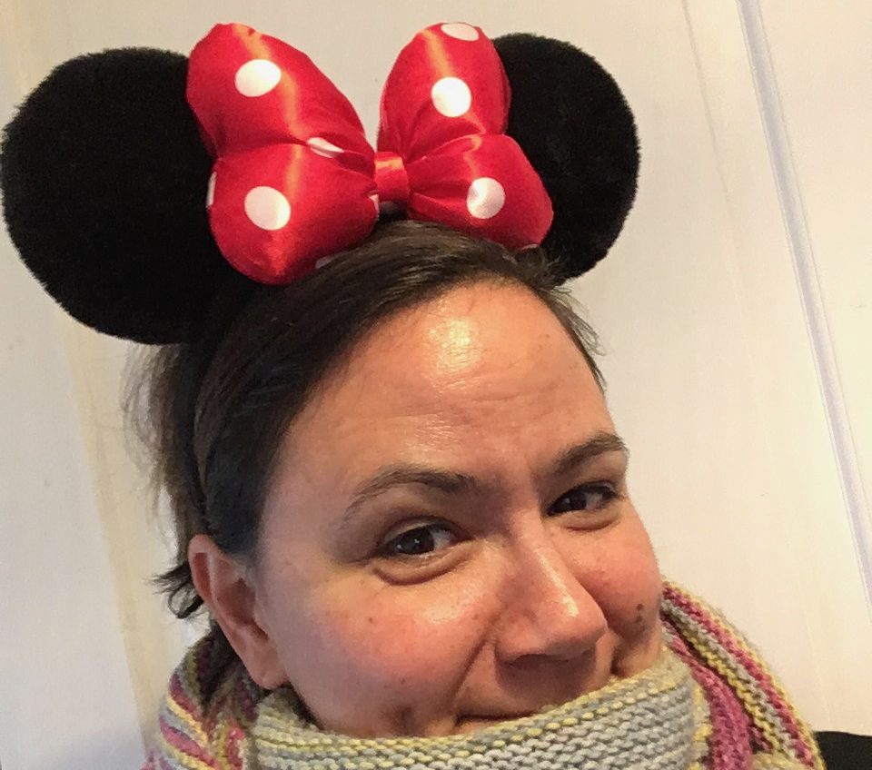 Sophie emmitouflée dans un châle avec un regard malicieux et des oreilles noires de Minnie assorties d'un gros nœud rouge à pois.
