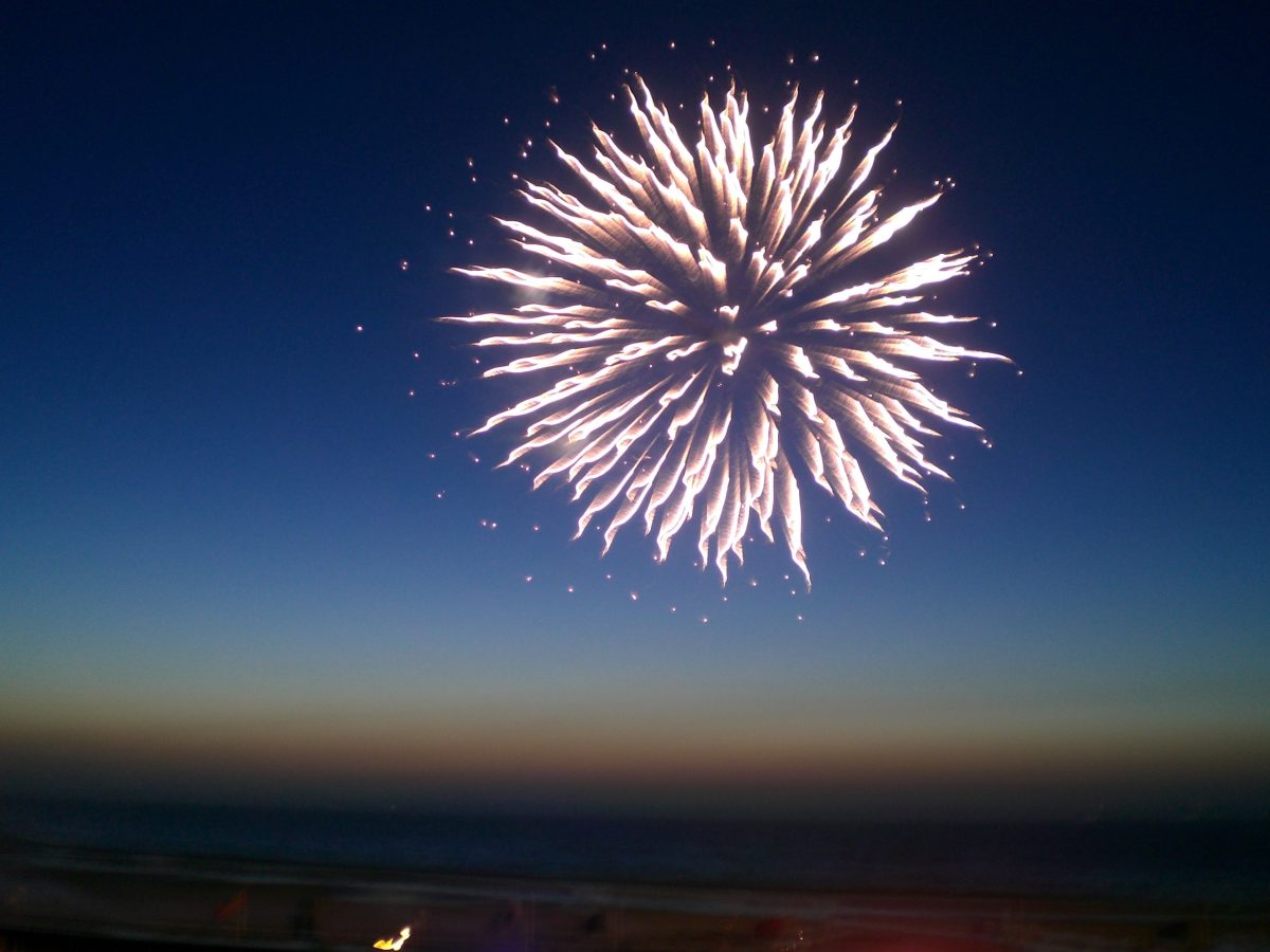 Feu d'artifice rose pâle qui éclate dans un ciel couchant en bord de mer