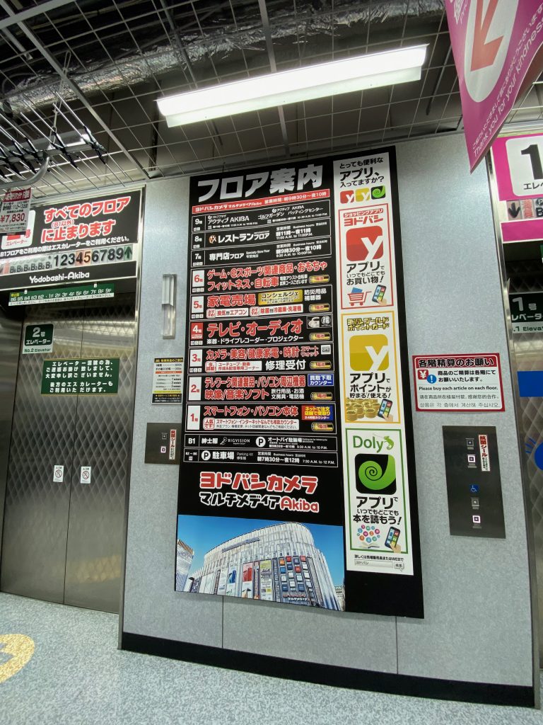 Panneau d'indication de chaque étage en japonais. Il y a 9 étages avec les caractères japonais qui indiquent par exemple l'électroménager, l'informatique, etc… Ils sont entourés de publicités.