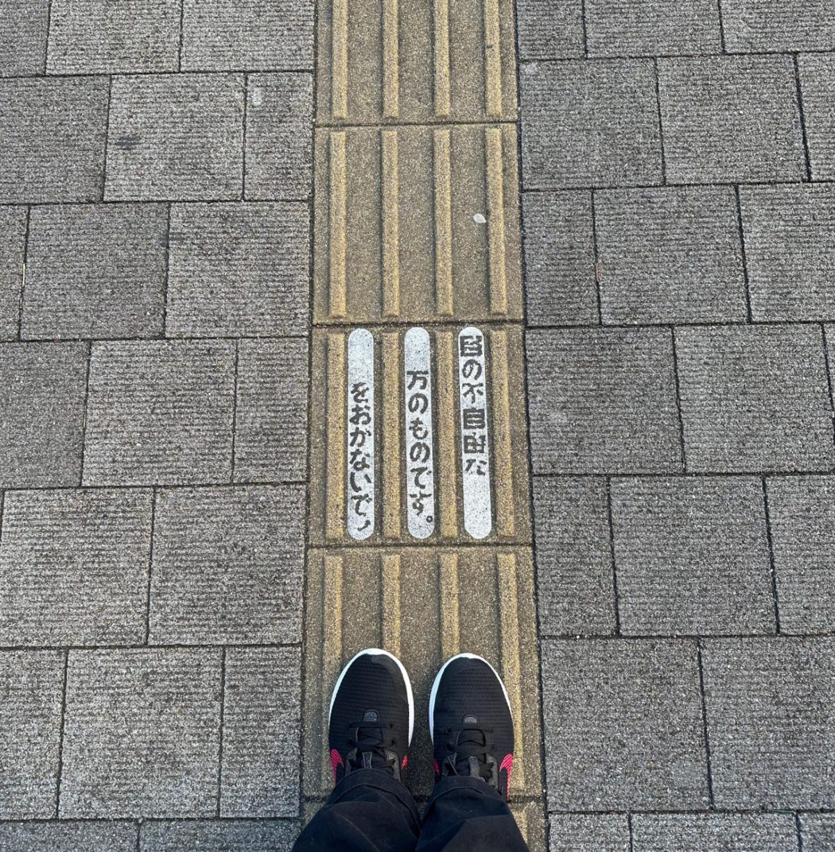 Mes baskets noires à pied joint sur une bande podotactile verticale et une inscription japonaise (j'attends la traduction)