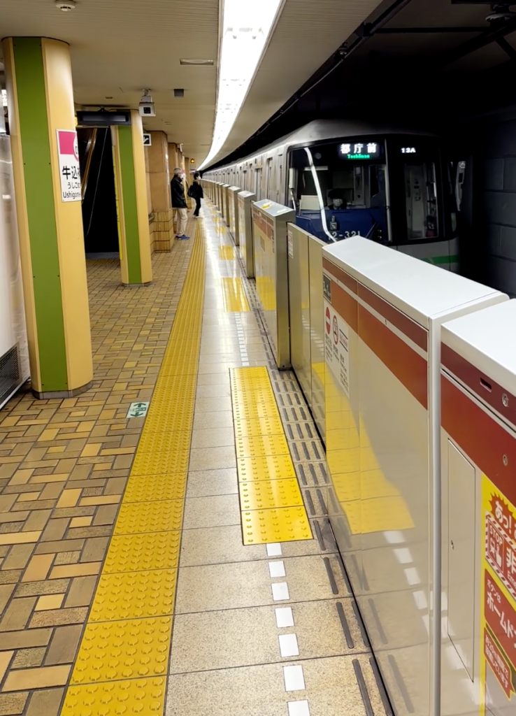 Métro qui entre en gare, avec une barrière métallique qui le sépare du quai. Au sol, on voit des bandes podotactiles tout le long du quai ainsi qu'à l'emplacement des portes.